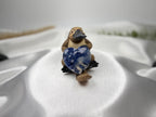 Treasured Energies polished blue and white sodalite crystal heart held by a small platypus figurine on white fabric.
