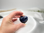 Treasured Energies polished blue and white sodalite crystal heart held in a hand against a white satin background.