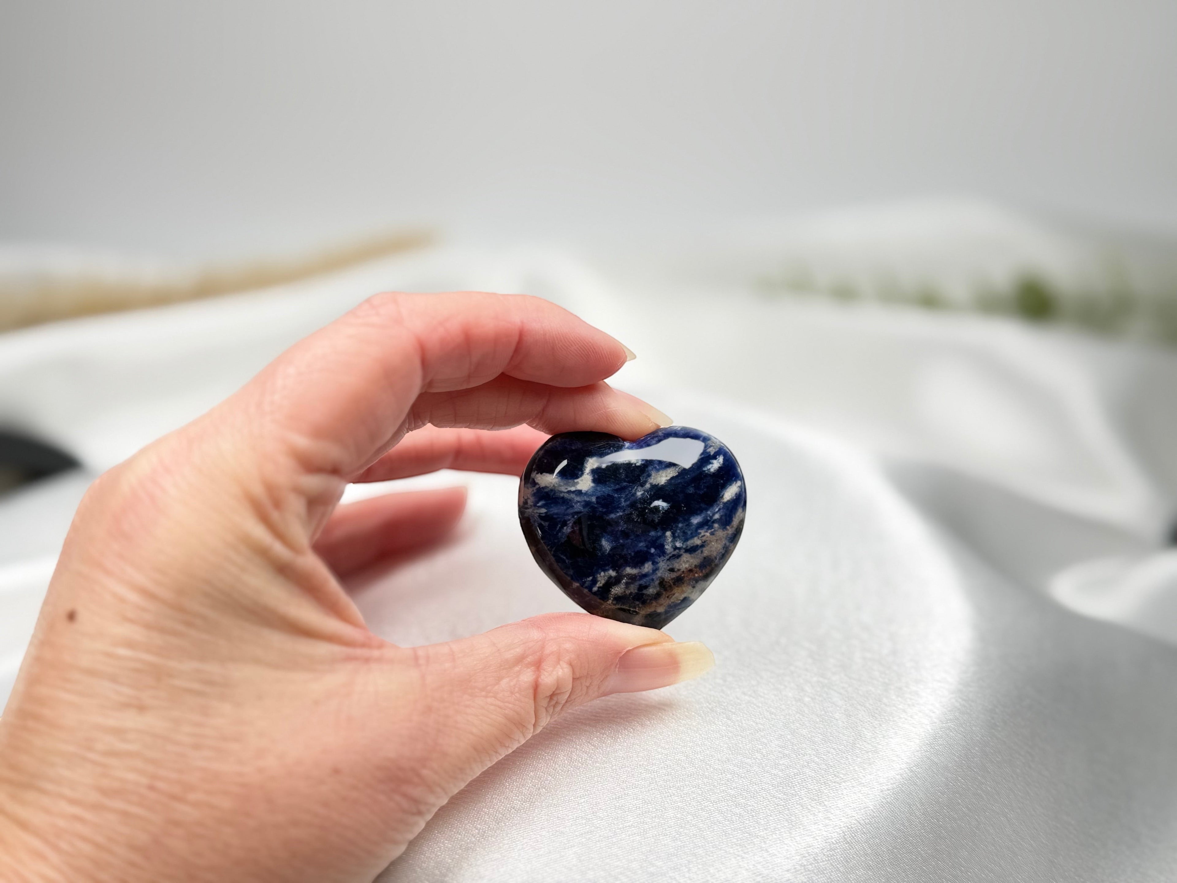 Treasured Energies polished blue and white sodalite crystal heart held in a hand against a white satin background.