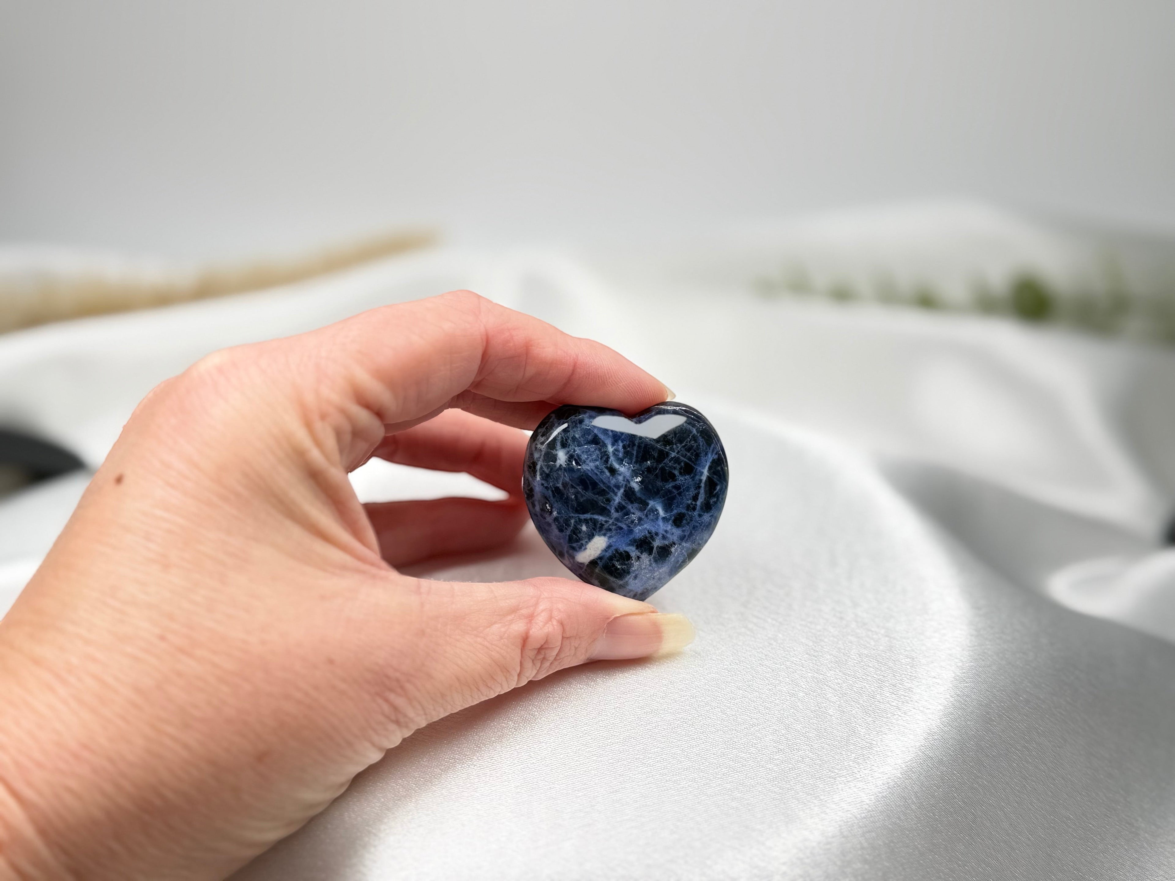 Treasured Energies polished blue sodalite crystal heart held in a hand against a soft white satin background.