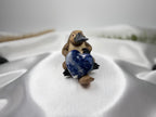 Treasured Energies polished blue Sodalite crystal heart held by a small platypus figurine on white satin fabric