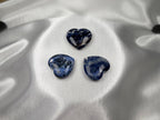 Three polished Treasured Energies sodalite crystal hearts with deep blue and white patterns on a satin fabric.