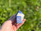 Treasured Energies sodalite crystal point with a polished tip and raw base held in a hand against a green background