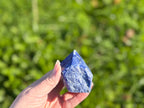 Treasured Energies Sodalite crystal point with a polished tip and raw base held in a hand against a green background