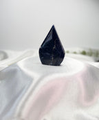 Treasured Energies polished royal blue Sodalite crystal  flame-shaped crystal sculpture on a white satin fabric background.