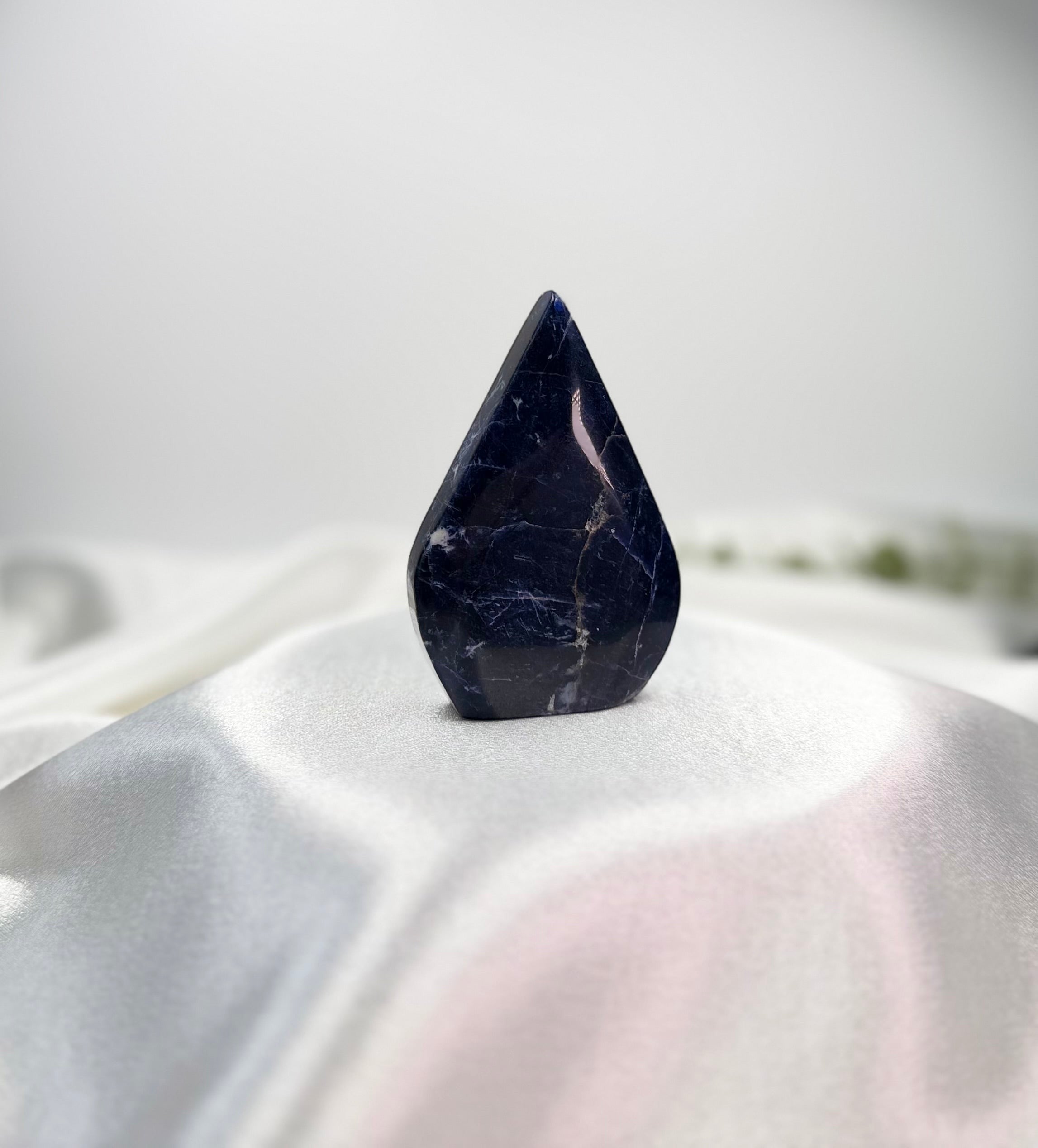 Treasured Energies polished royal blue Sodalite flame-shaped crystal sculpture on a white satin display stand.
