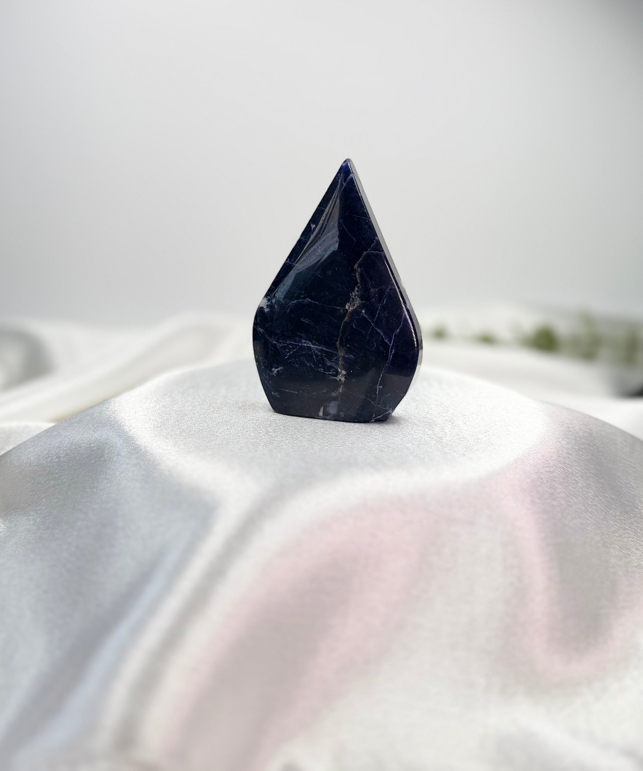 Treasured Energies polished royal blue Sodalite crystal flame freestanding form on a white satin fabric background.