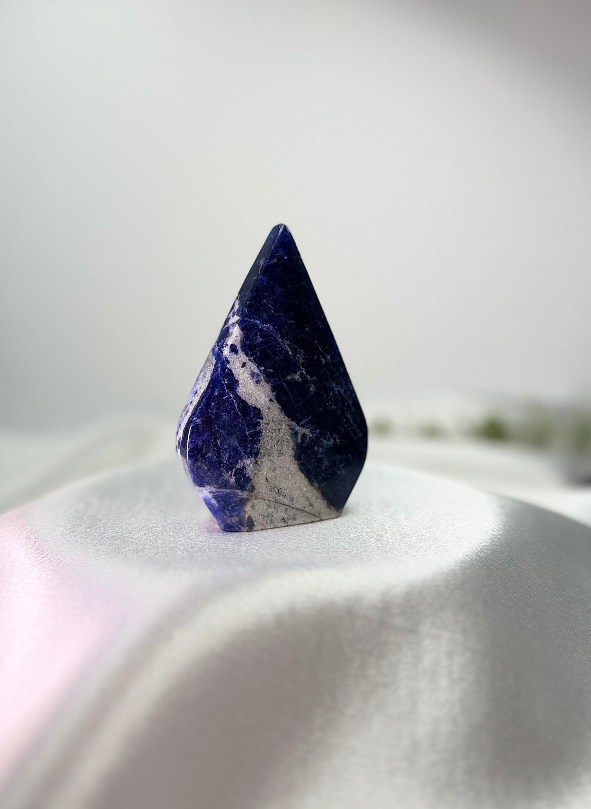Treasured Energies polished royal blue Sodalite flame freeform crystal with white mineral inclusions on white fabric.