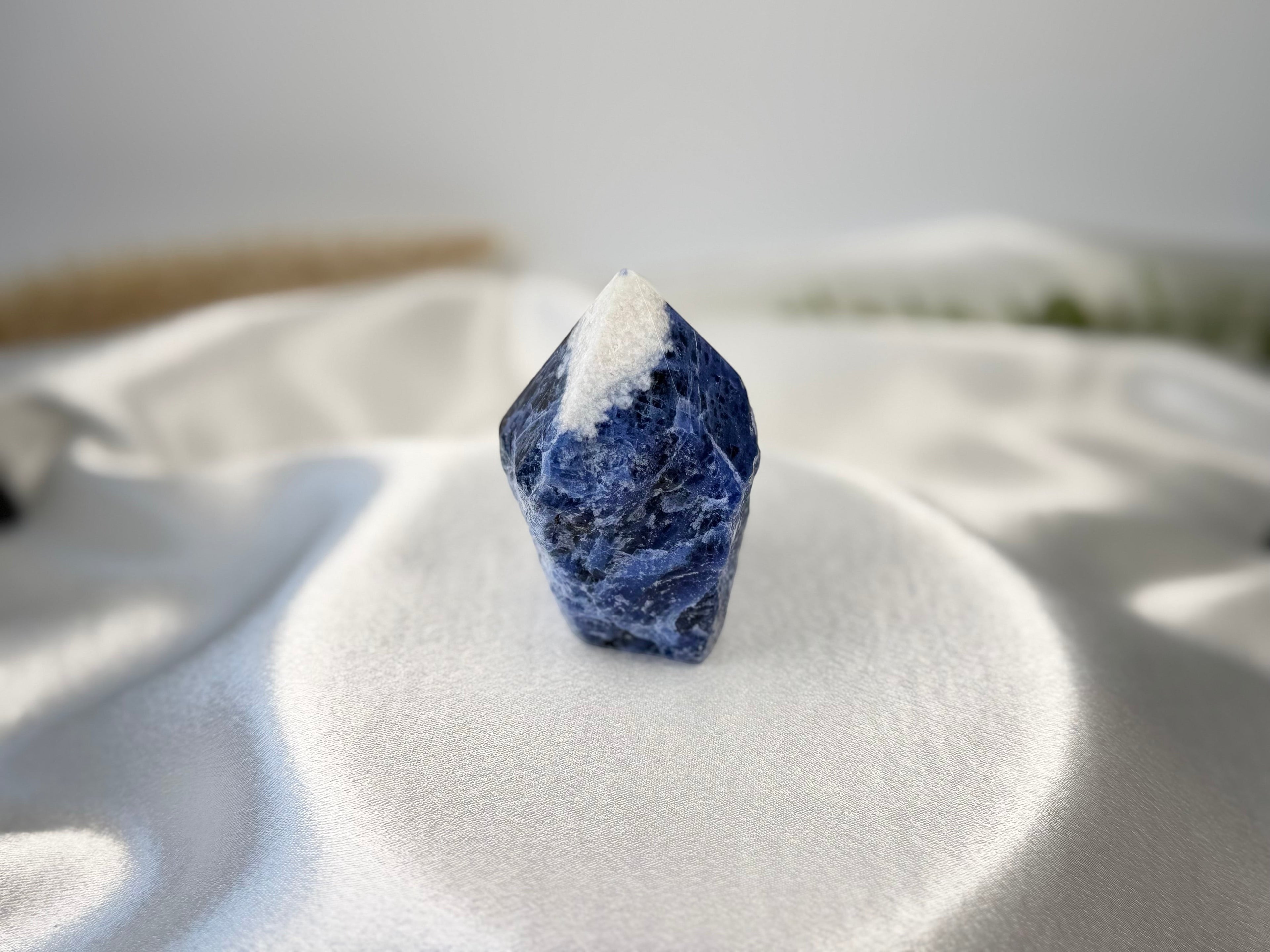 Treasured Energies sodalite crystal tower with a raw base and polished point on a white satin fabric background.