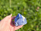 Treasured Energies Sodalite crystal point with a polished top and raw base held in a hand against a green background.