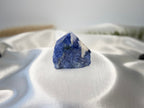 Treasured Energies Sodalite crystal point with a polished top and raw, natural base on a white satin background.