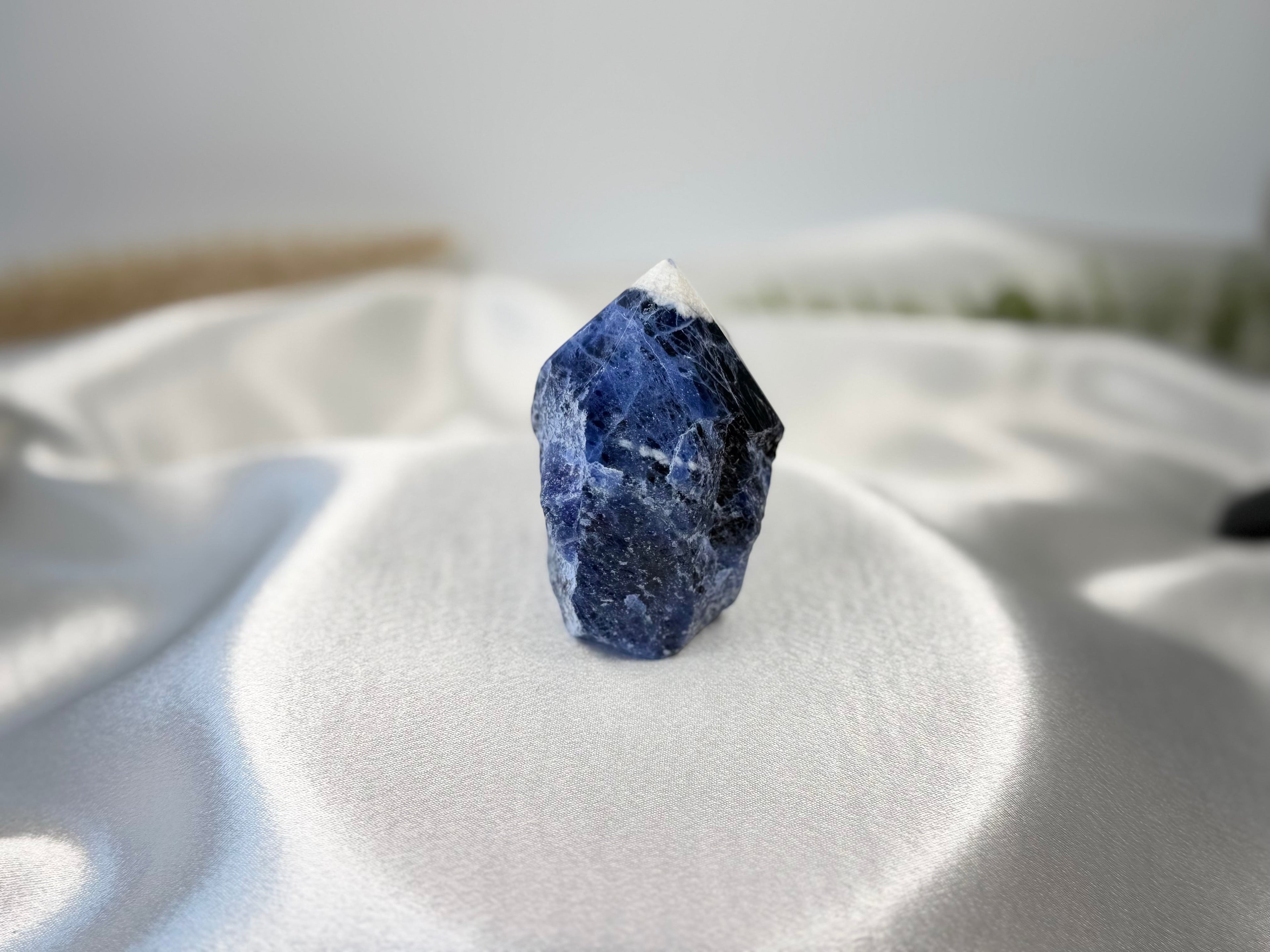 Treasured Energies Sodalite crystal tower with a polished point and raw base on a white satin background