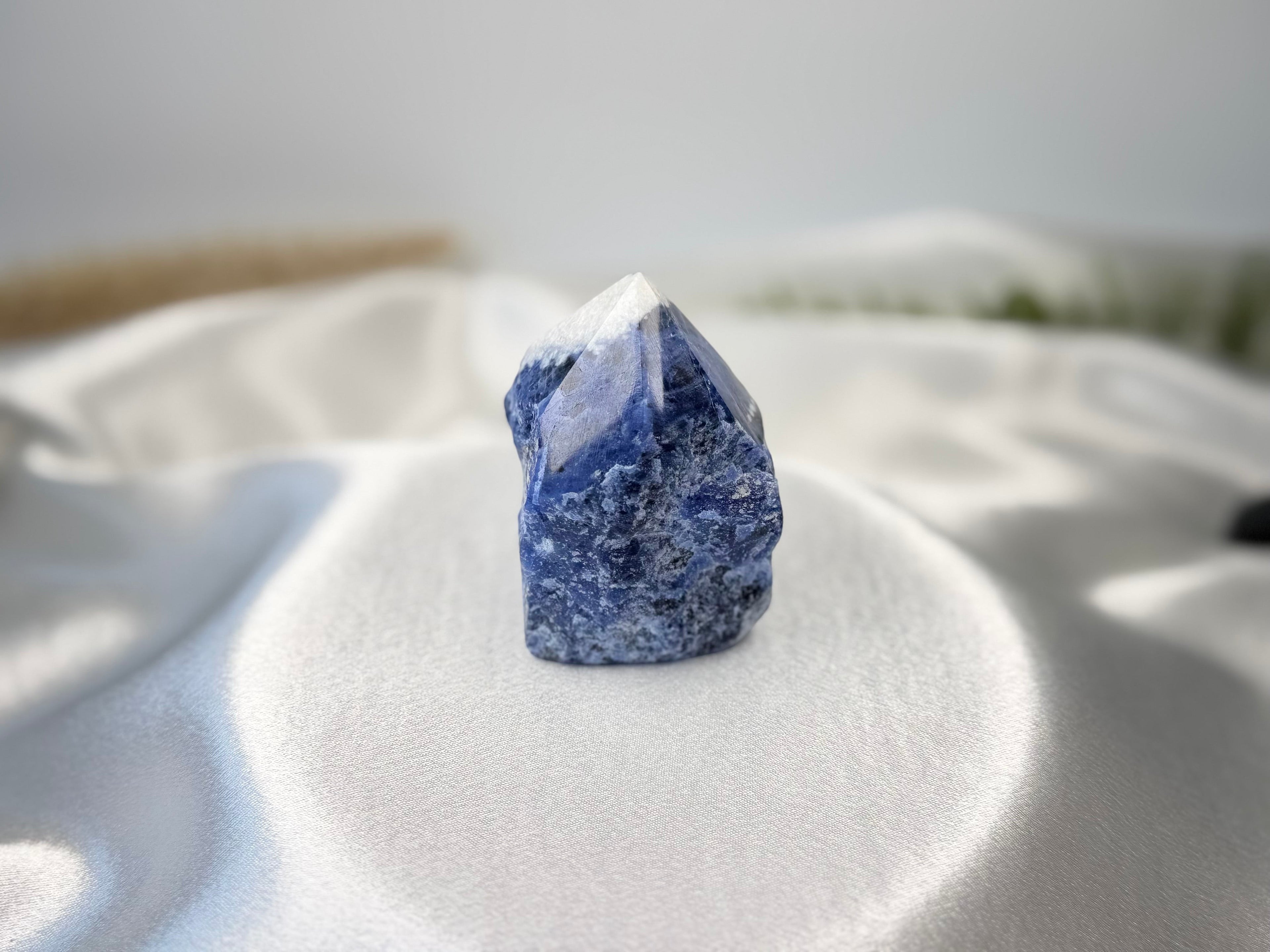 Treasured Energies Sodalite crystal tower with a polished point and raw base on a white satin fabric background.