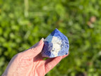 Treasured Energies sodalite crystal tower with a polished point and raw base held in a hand against a green background.