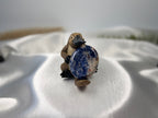 Treasured Energies blue and white Sodalite worry stone held by a small platypus figurine on a white satin fabric
