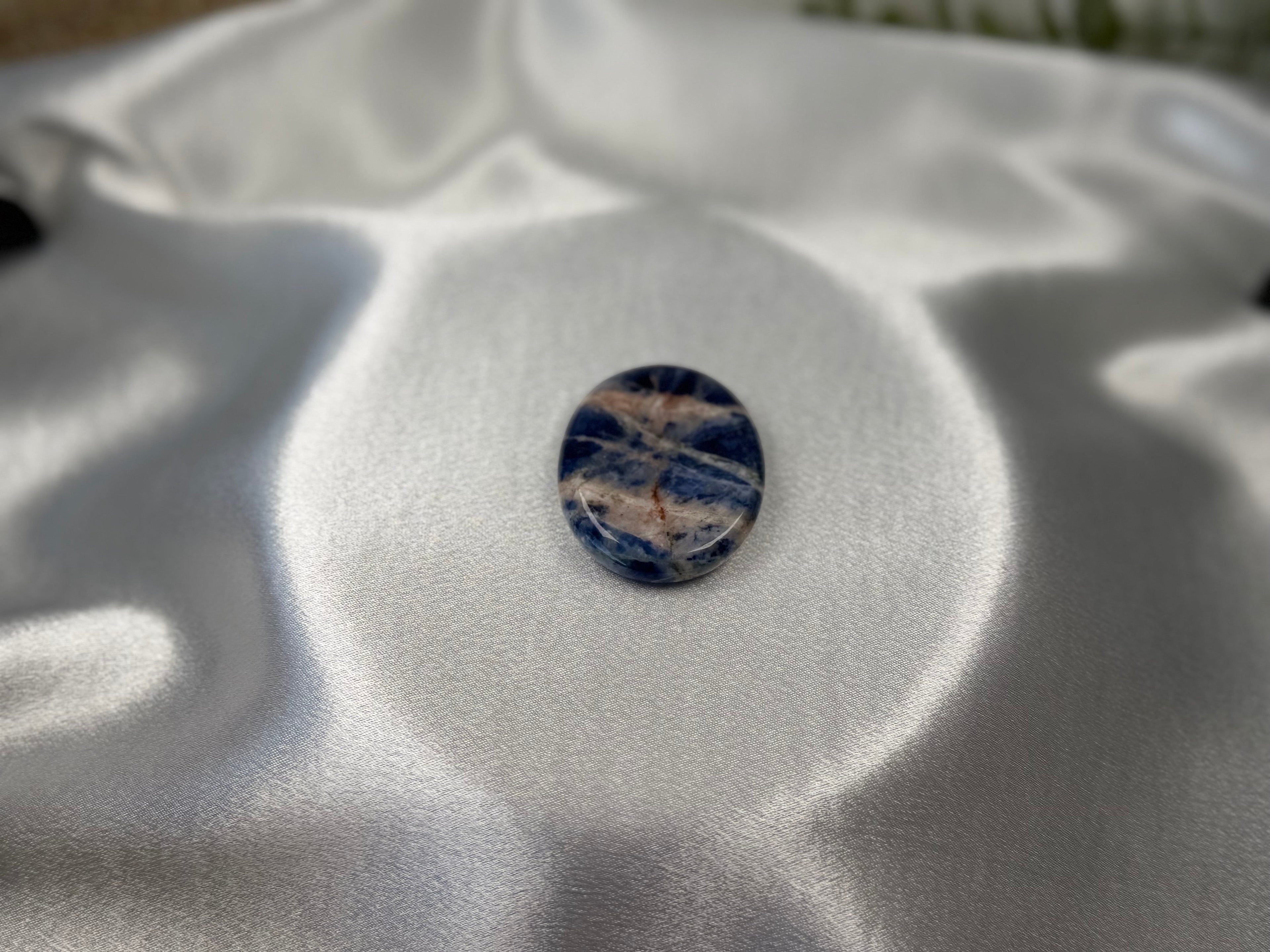 Treasured Energies smooth oval Sodalite worry stone with deep blue and white mineral patterns on a satin fabric.