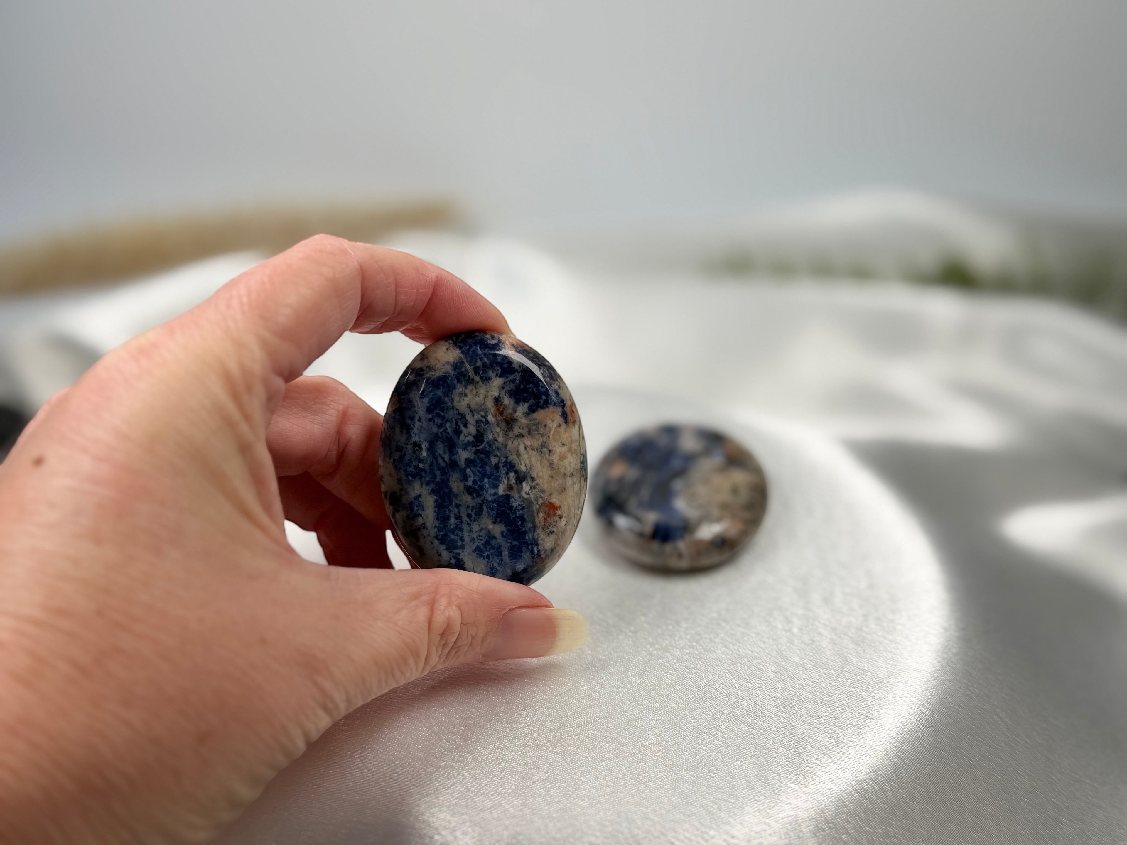 Treasured Energies smooth, oval Sodalite worry stone with royal blue and white patterns held in a hand.