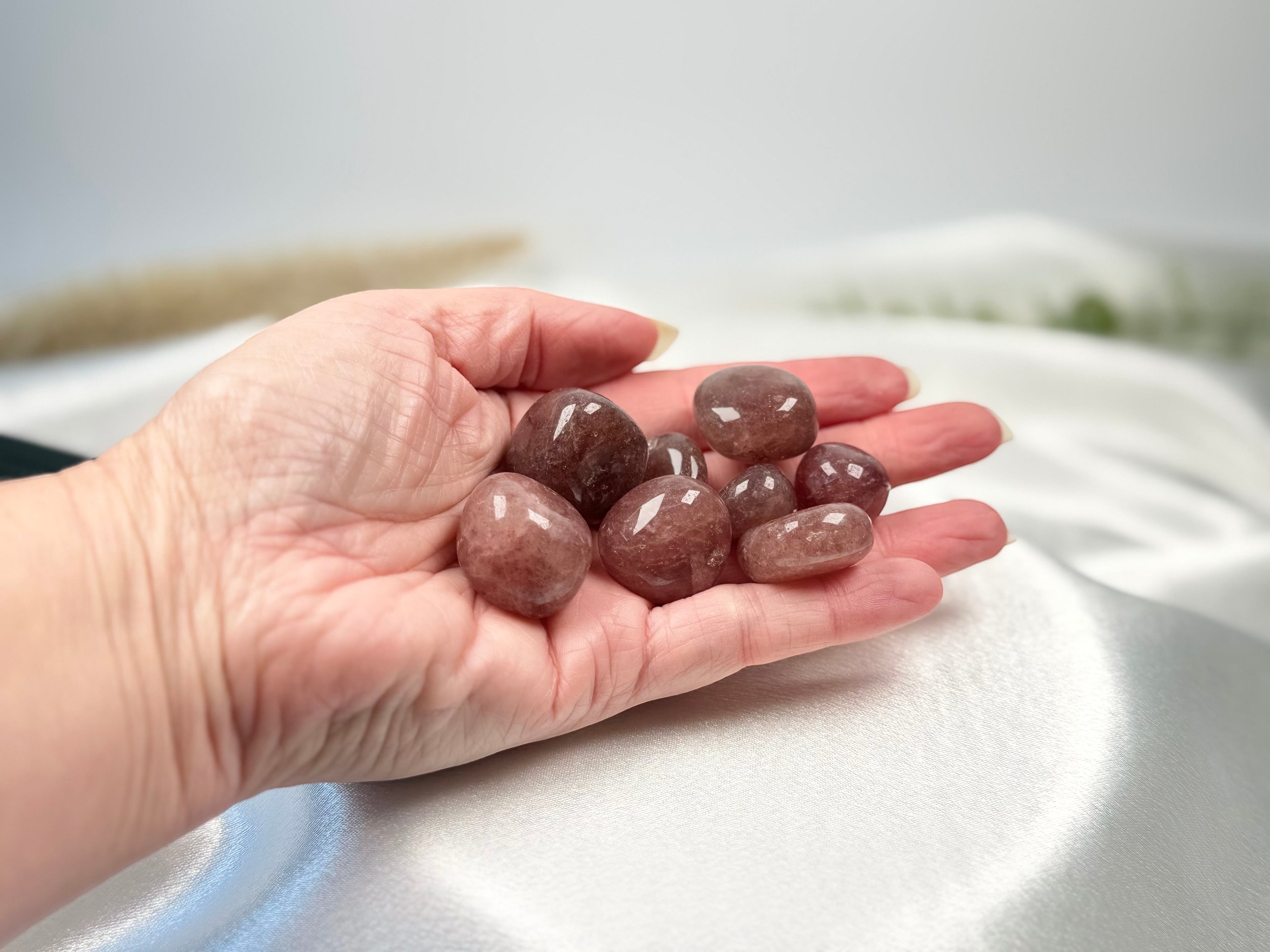 Treasured Energies polished strawberry quartz tumbled stones held in a palm against a soft white satin background