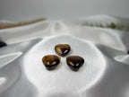 Treasured Energies polished tiger eye crystal hearts with golden brown chatoyant bands on a white satin background.