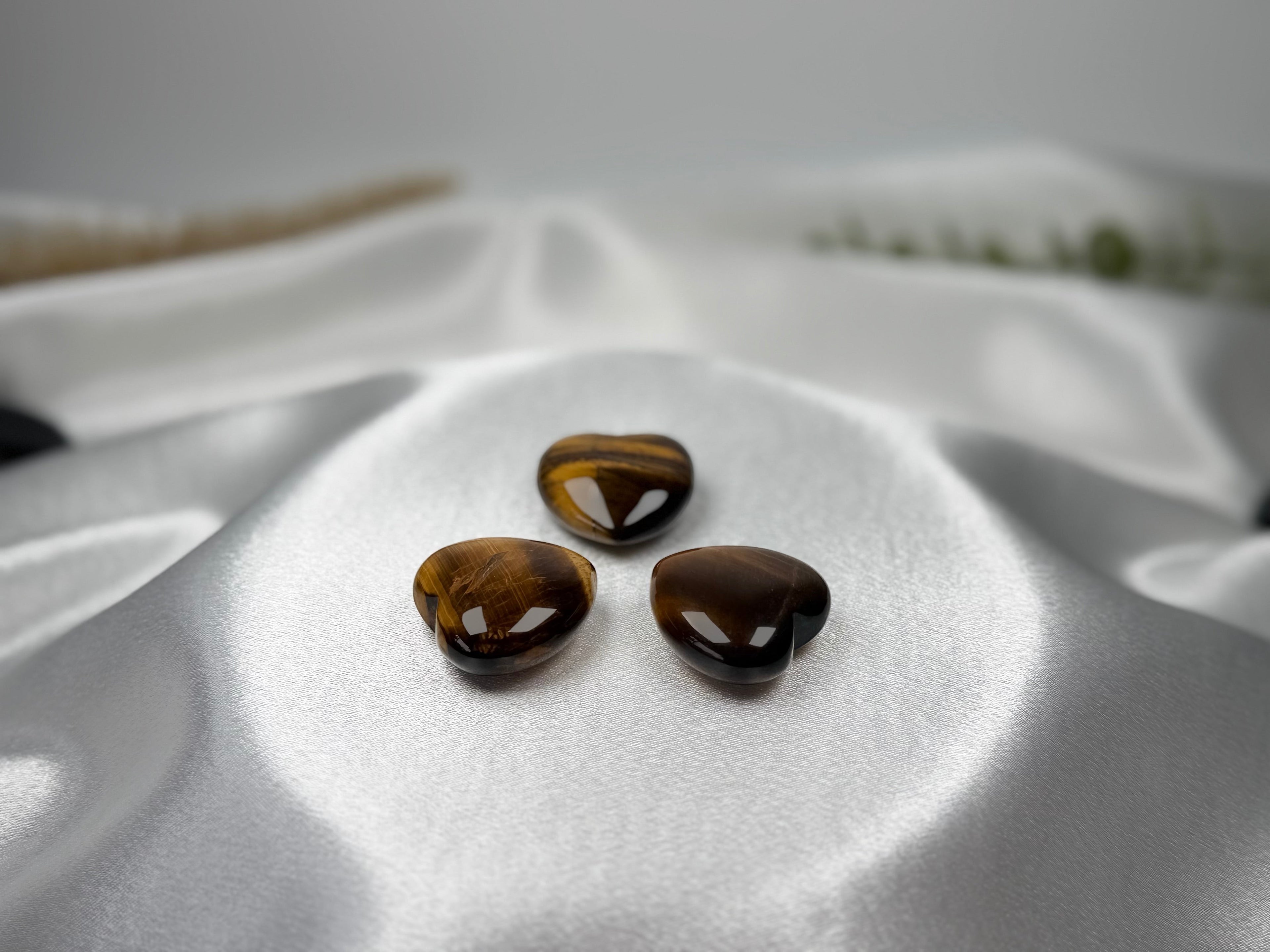 Treasured Energies polished tiger eye crystal hearts with golden brown chatoyant bands on a white satin background.