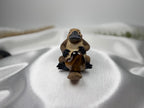 Treasured Energies polished brown tiger eye crystal heart held by a small carved platypus figurine on white fabric.