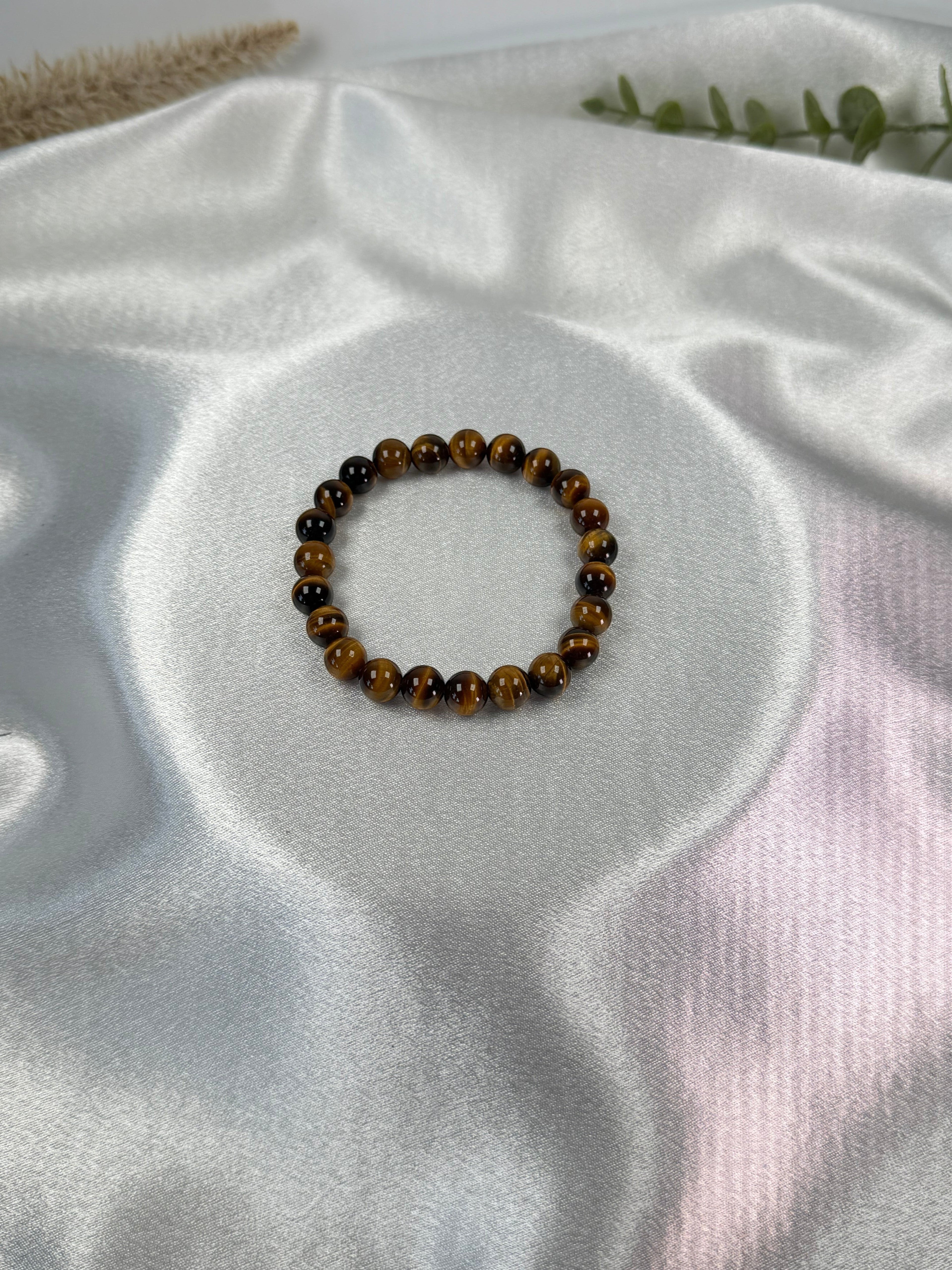 Treasured Energies gold tiger eye crystal bead bracelet on a smooth white satin fabric background.