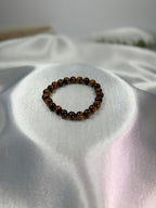 Treasured Energies gold tiger eye crystal bead bracelet resting on a smooth white satin fabric background.