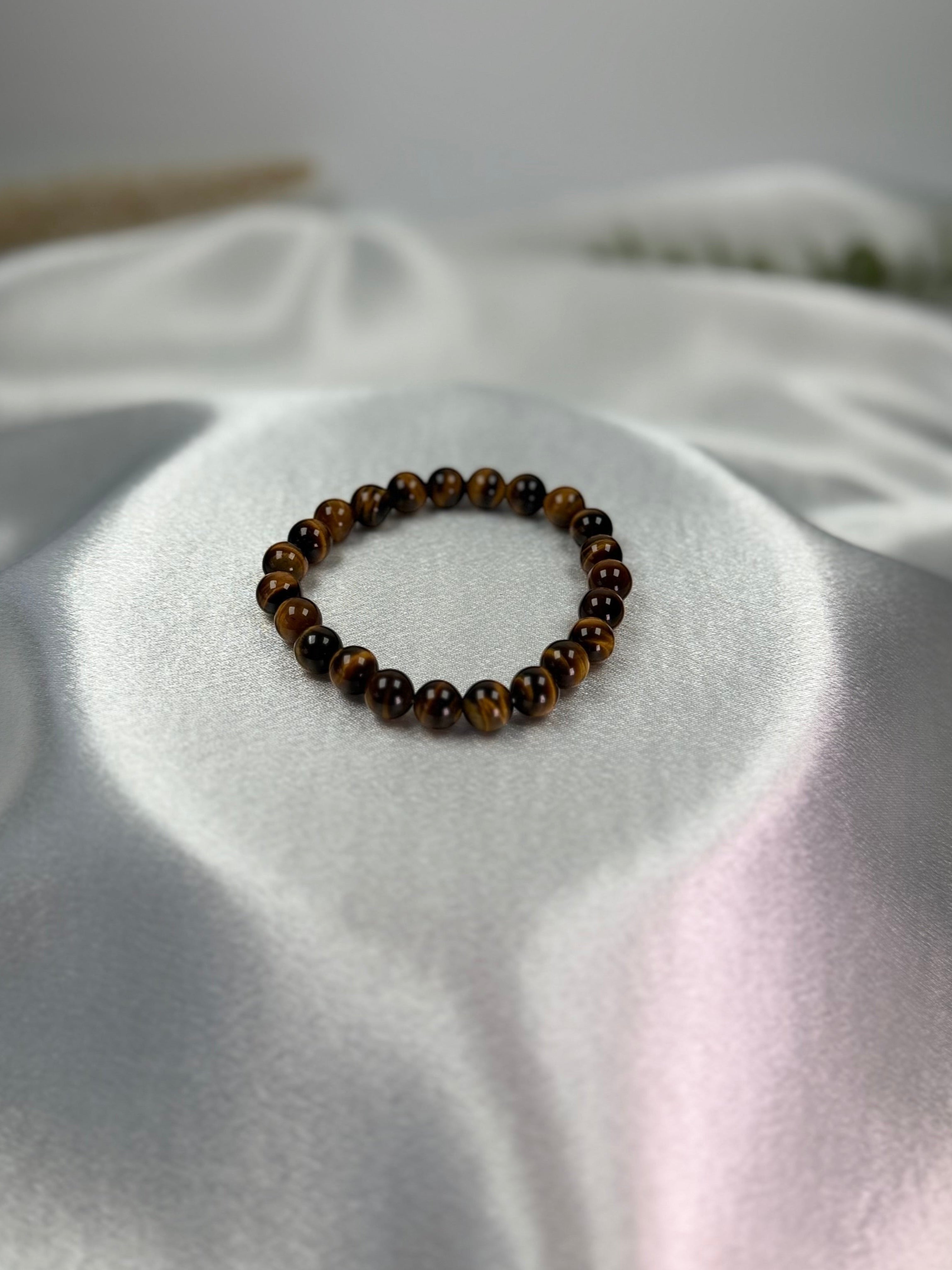 Treasured Energies gold tiger eye crystal bead bracelet resting on a smooth white satin fabric background.