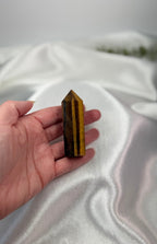 Treasured Energies Tigers Eye crystal tower held in a hand against a soft white satin background.