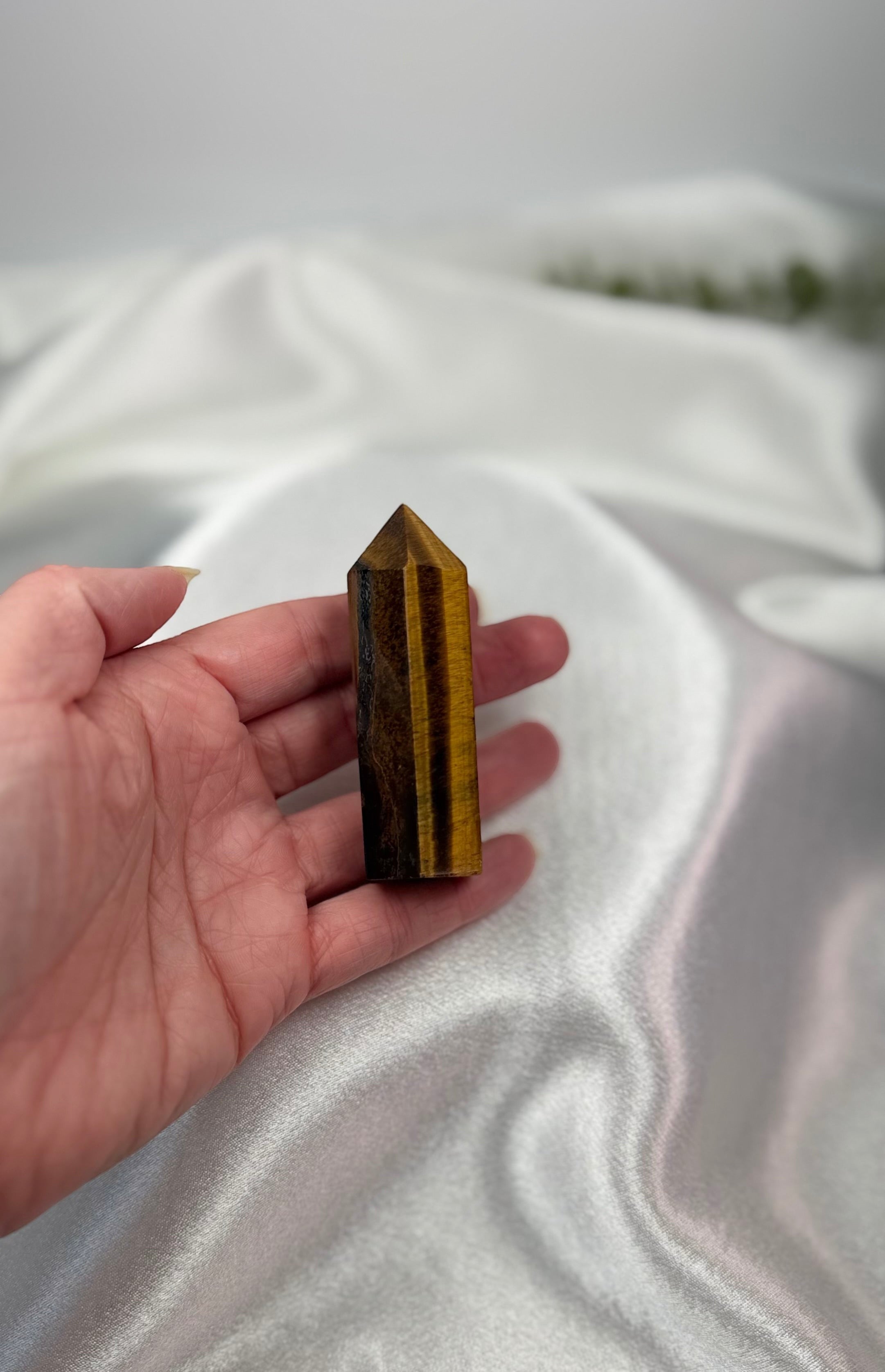 Treasured Energies Tigers Eye crystal tower held in a hand against a soft white satin background.