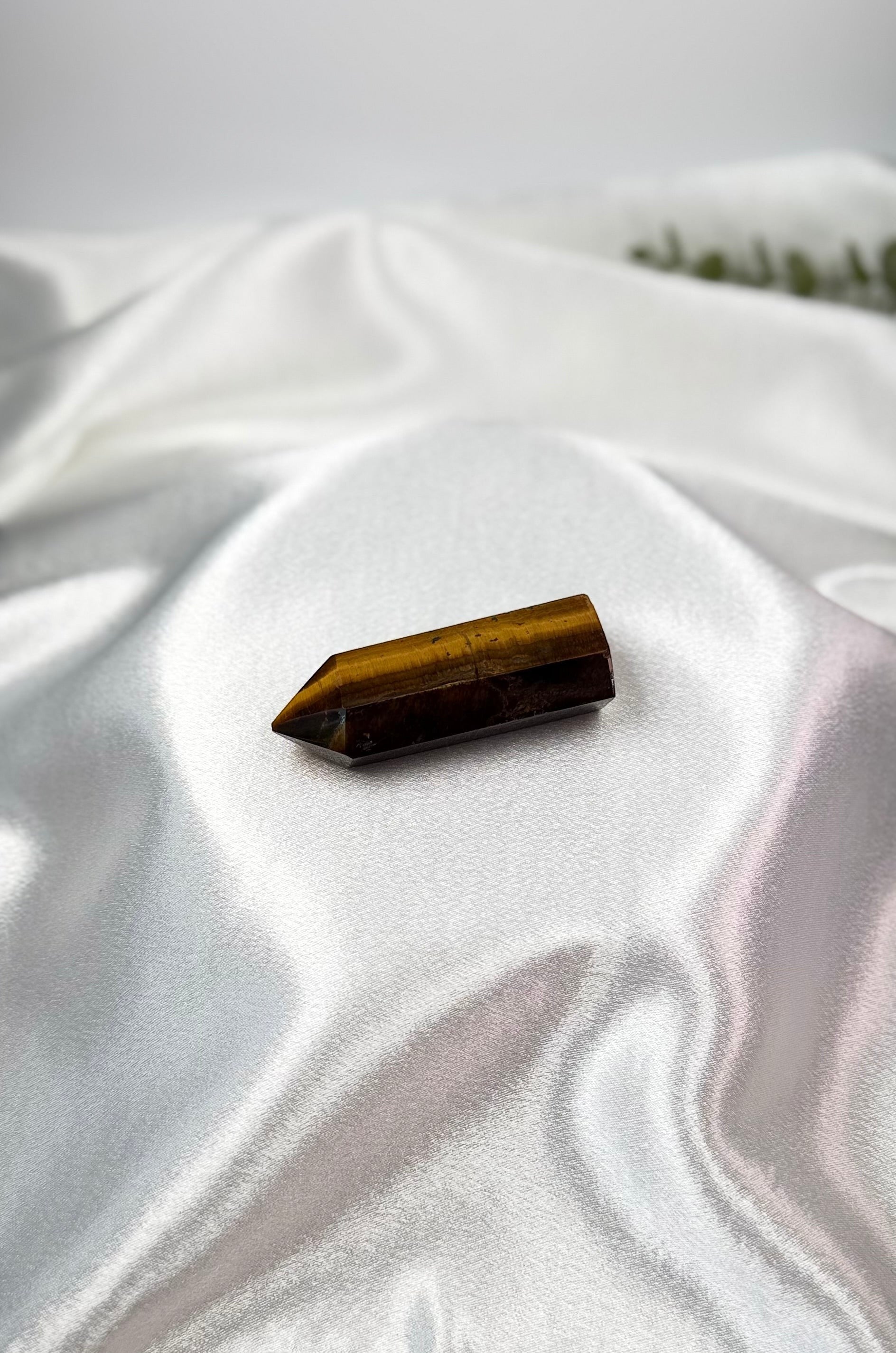 Treasured Energies polished Tigers Eye crystal tower with golden-brown chatoyant bands on a white satin background.
