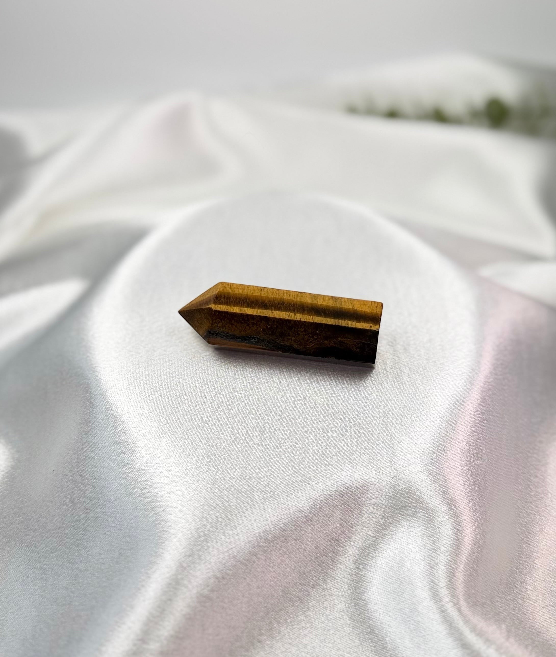 Treasured Energies polished Tigers Eye crystal tower with golden-brown chatoyant bands on a white satin background.