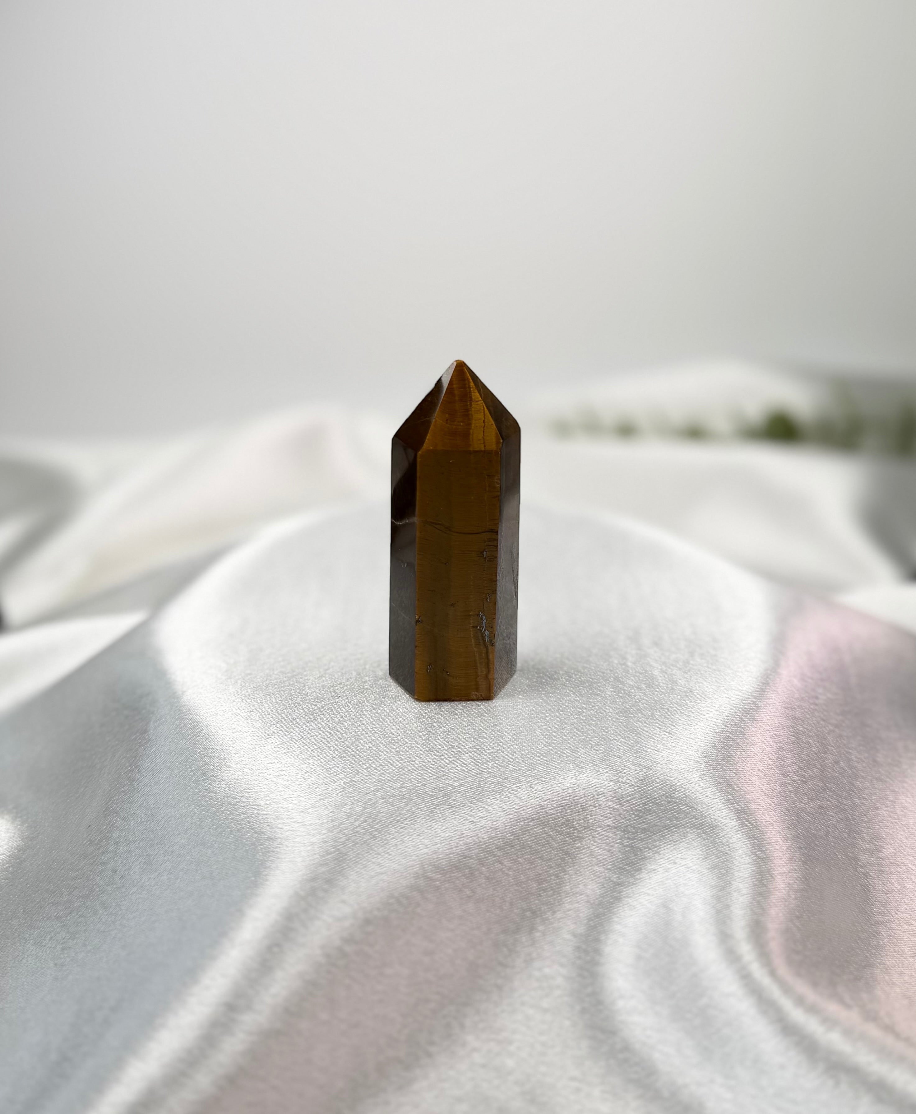 Treasured Energies polished Tigers Eye crystal tower with a pointed tip on white satin fabric.