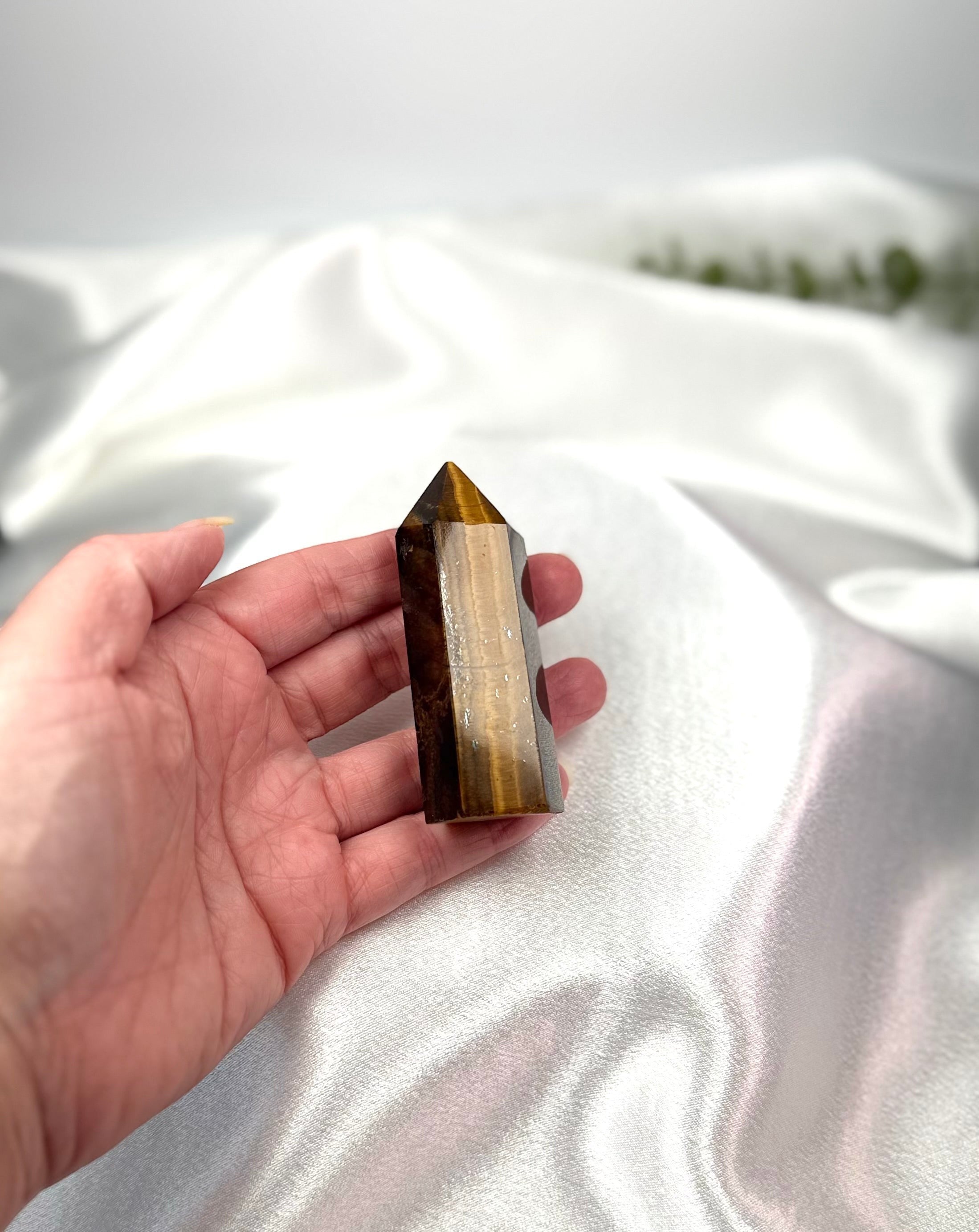 Treasured Energies Tigers Eye crystal tower held in a hand against a white satin background.