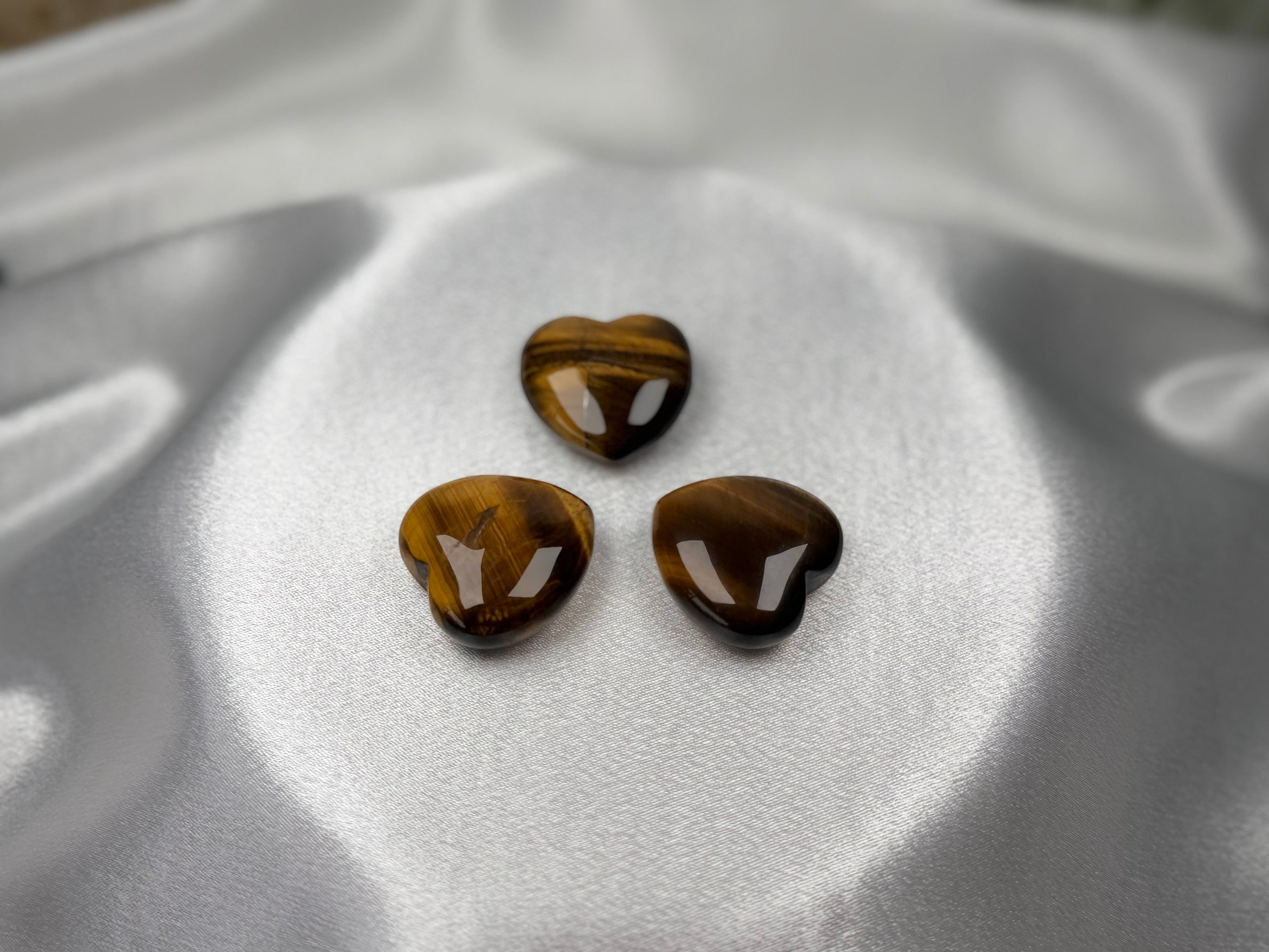 Three polished heart-shaped Tiger Eye crystals with golden-brown chatoyant bands from Treasured Energies