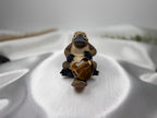 Treasured Energies polished brown tigers eye crystal heart held by a small platypus figurine on white satin fabric