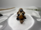 Treasured Energies polished brown Tiger Eye crystal heart held by a small decorative platypus figurine on white silk.