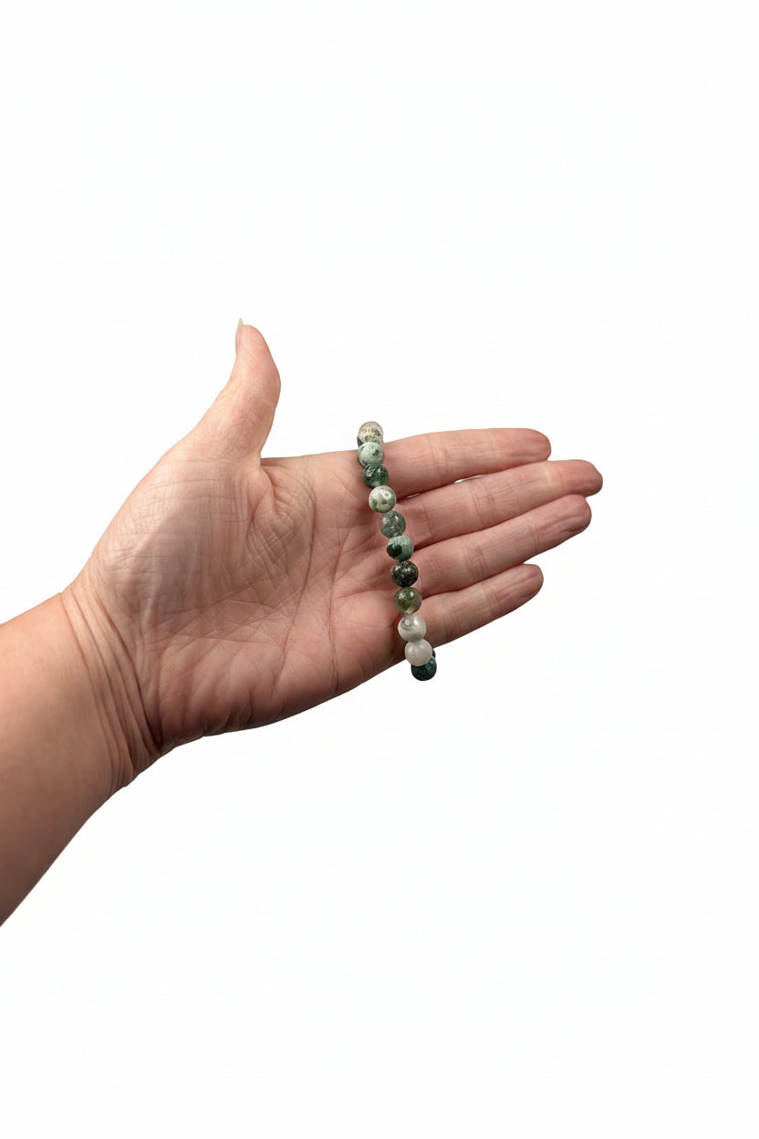 Treasured Energies tree agate crystal bead bracelet held in a palm against a soft white satin background