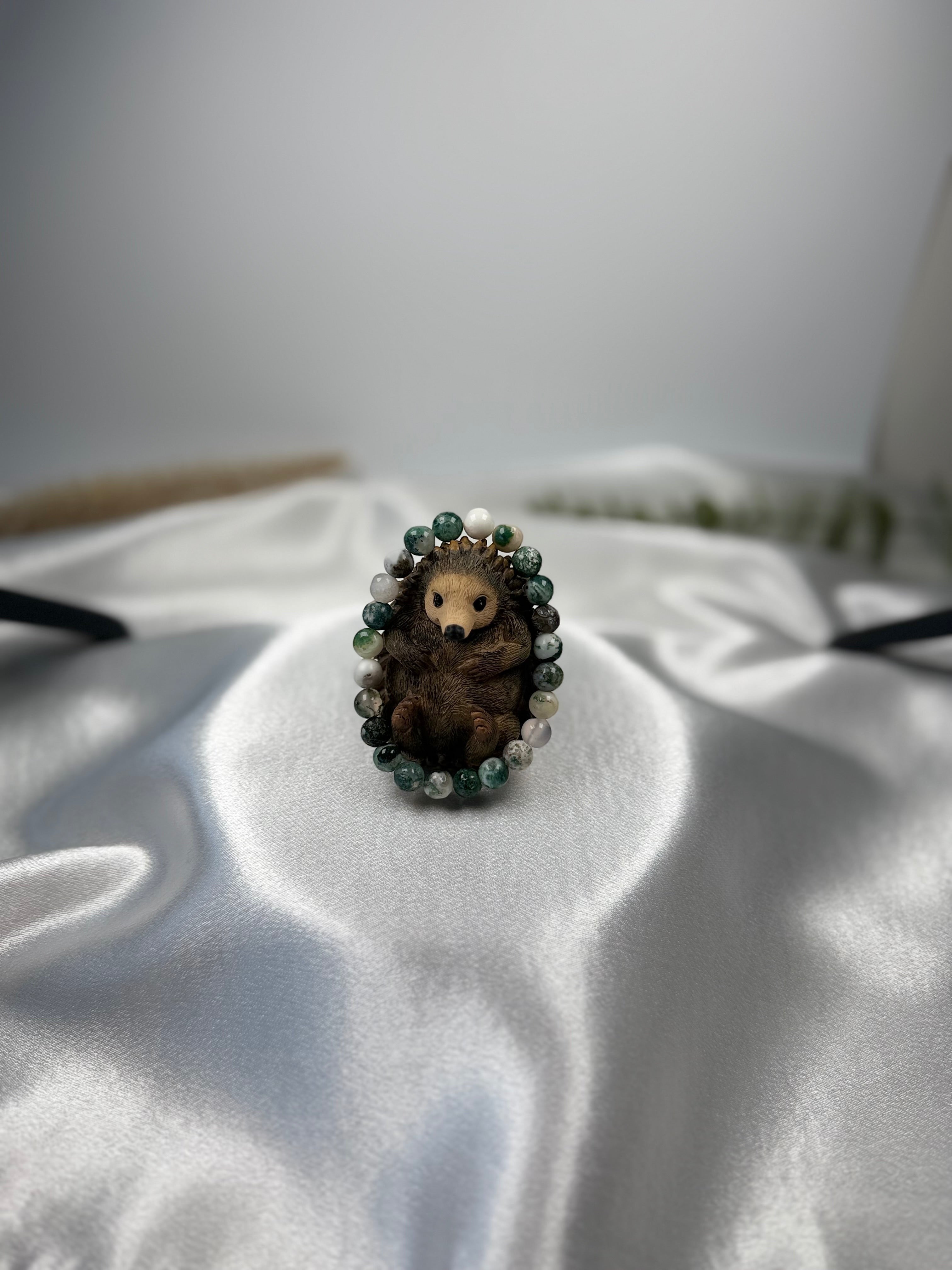 Treasured Energies Tree Agate crystal bead bracelet encircling a small decorative hedgehog figurine on white satin