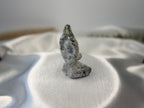 Treasured Energies tree agate yoga woman carving with white and green dendritic patterns on a white satin background.