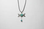 Treasured Energies Triple Moon pendant necklace with turquoise stones on a black cord against a textured grey fabric.