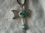 Treasured Energies Triple Moon Goddess pendant necklace with turquoise stones on a black cord against textured fabric