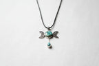 Treasured Energies Triple Moon pendant necklace with turquoise stones on a black cord against a textured grey fabric.