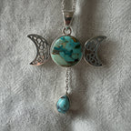 Treasured Energies Triple Moon pendant with turquoise stone and dangling teardrop on a textured grey background