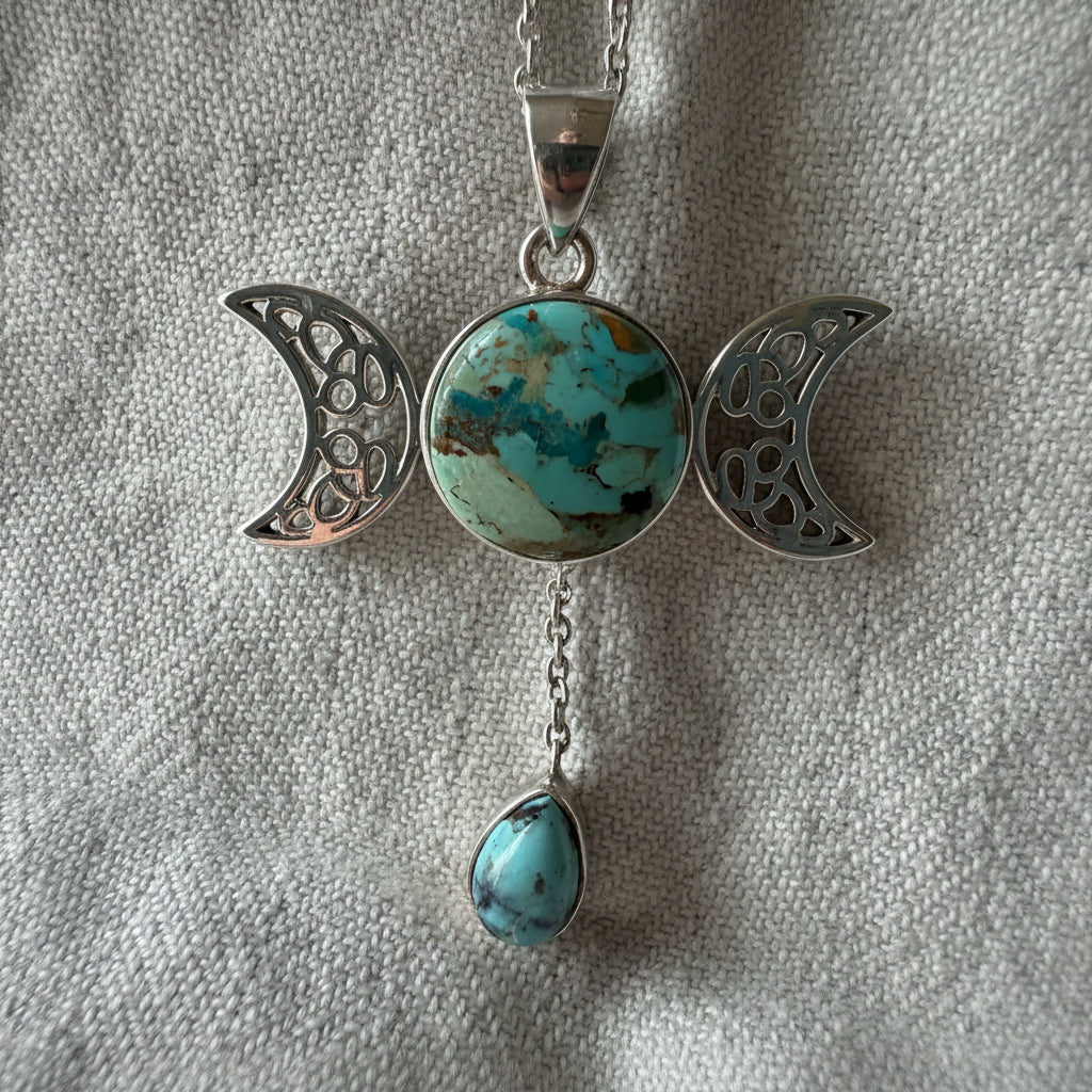 Treasured Energies Triple Moon pendant with turquoise stone and dangling teardrop on a textured grey background