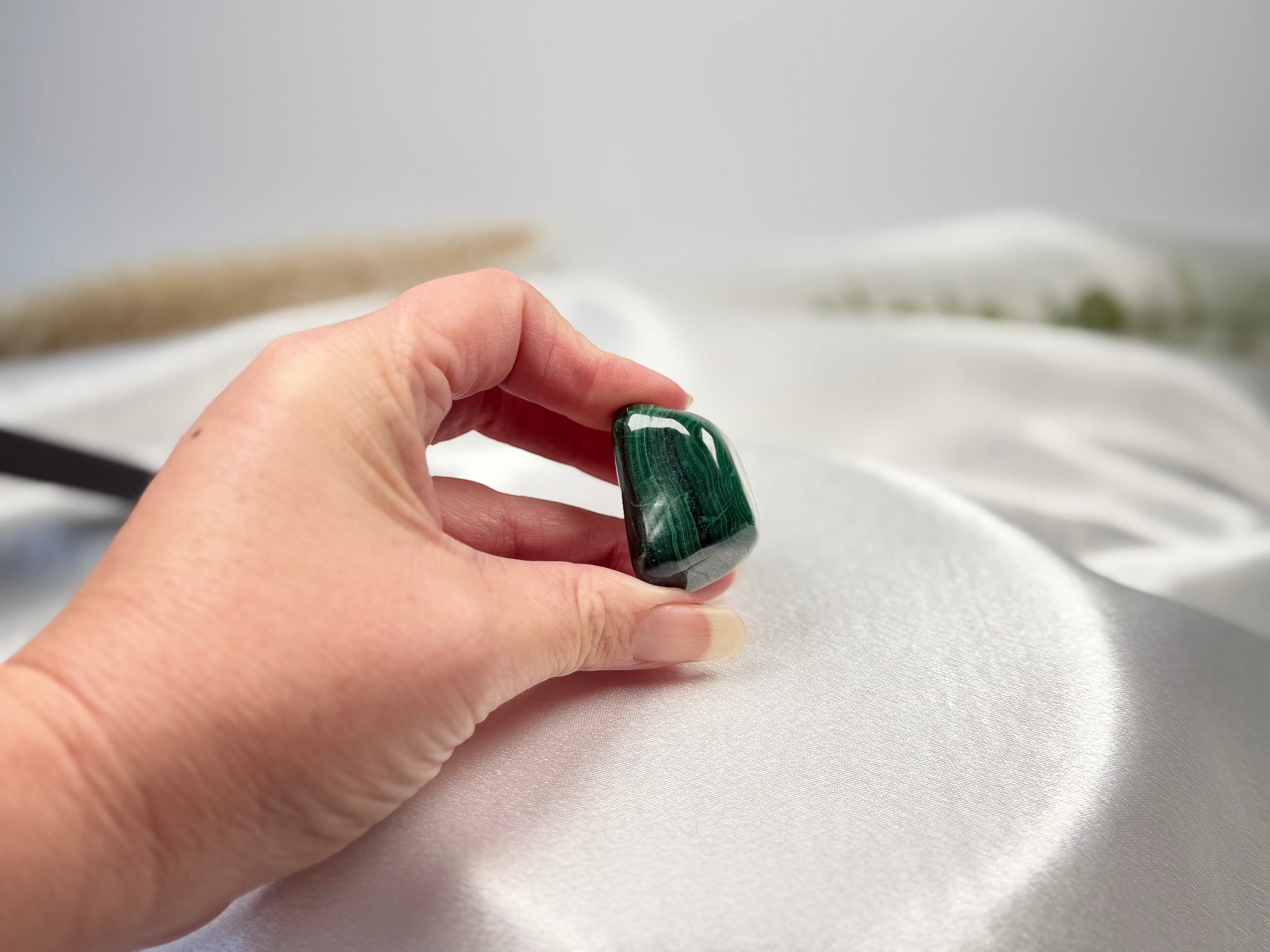 Treasured Energies high grade tumbled Malachite stone with deep green banding held in a hand against white silk