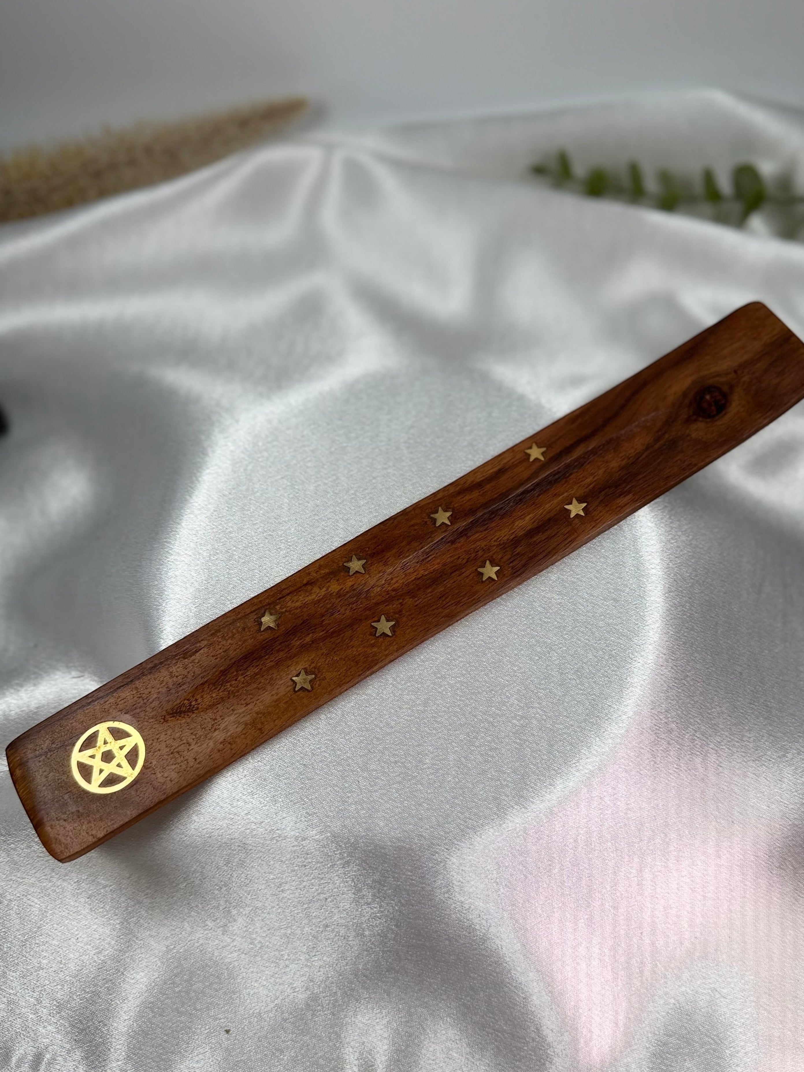 Treasured Energies wooden incense holder featuring a gold pentagram and star inlay on a white satin background.