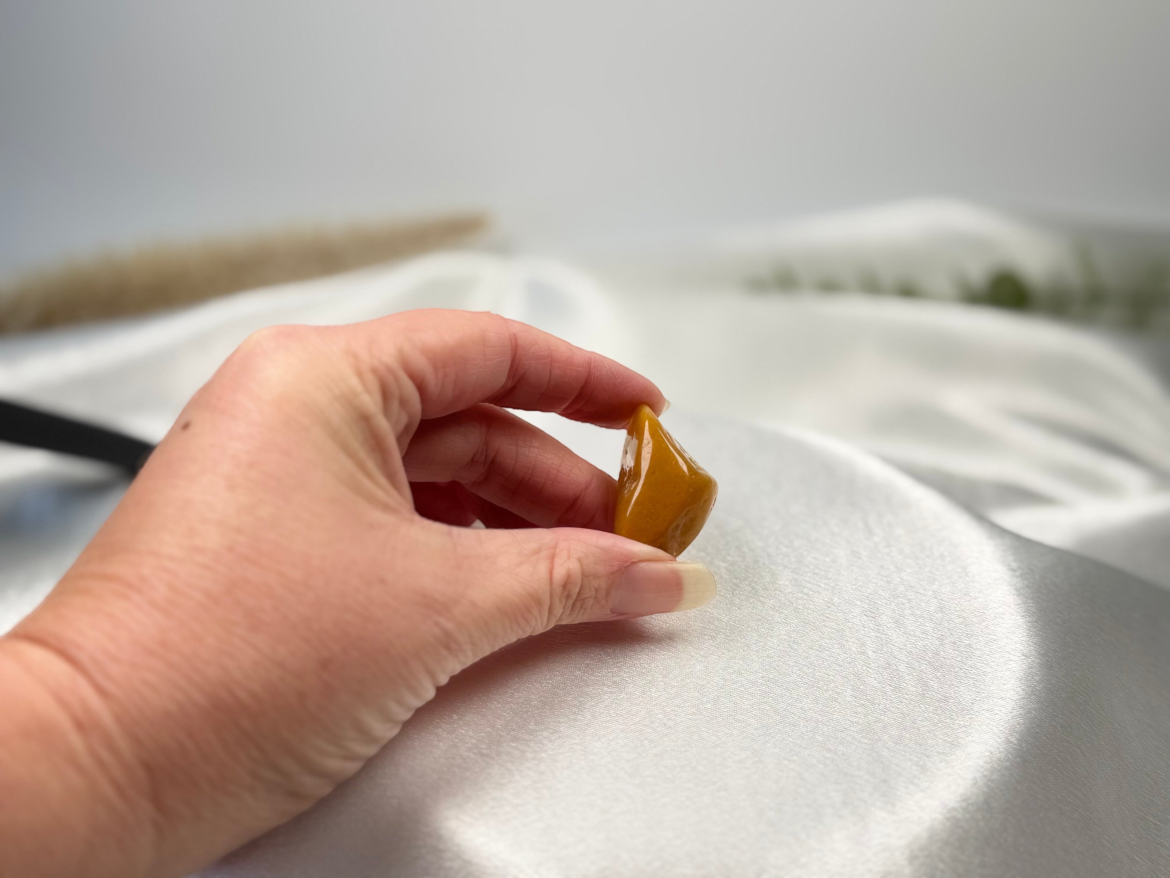 Treasured Energies yellow aventurine tumbled stone held in a hand against a white satin background