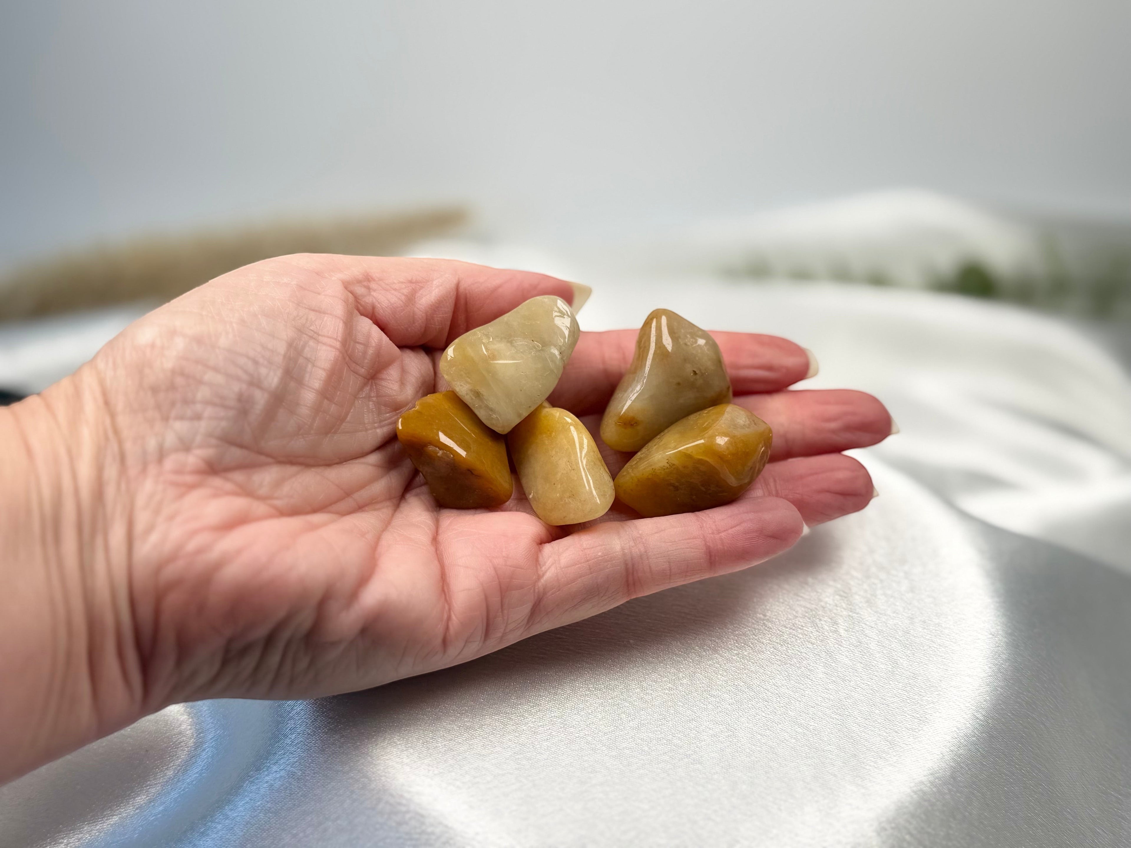 Treasured Energies yellow aventurine tumbled crystals held in a palm against a white satin background