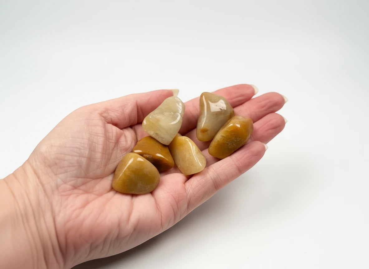 Treasured Energies yellow aventurine tumbled stones held in a palm, showcasing smooth golden quartz crystals.